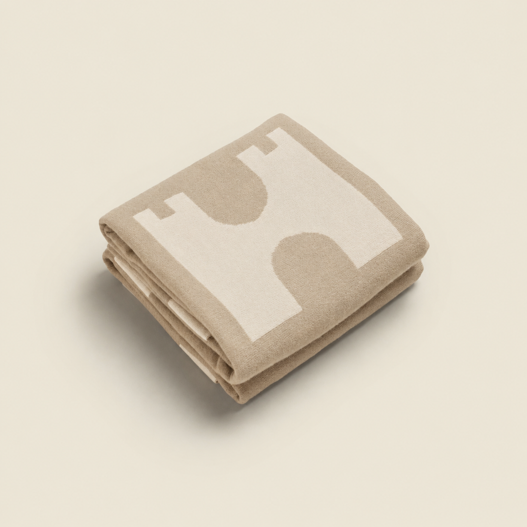 Folded beige blanket with a white logo on a beige background