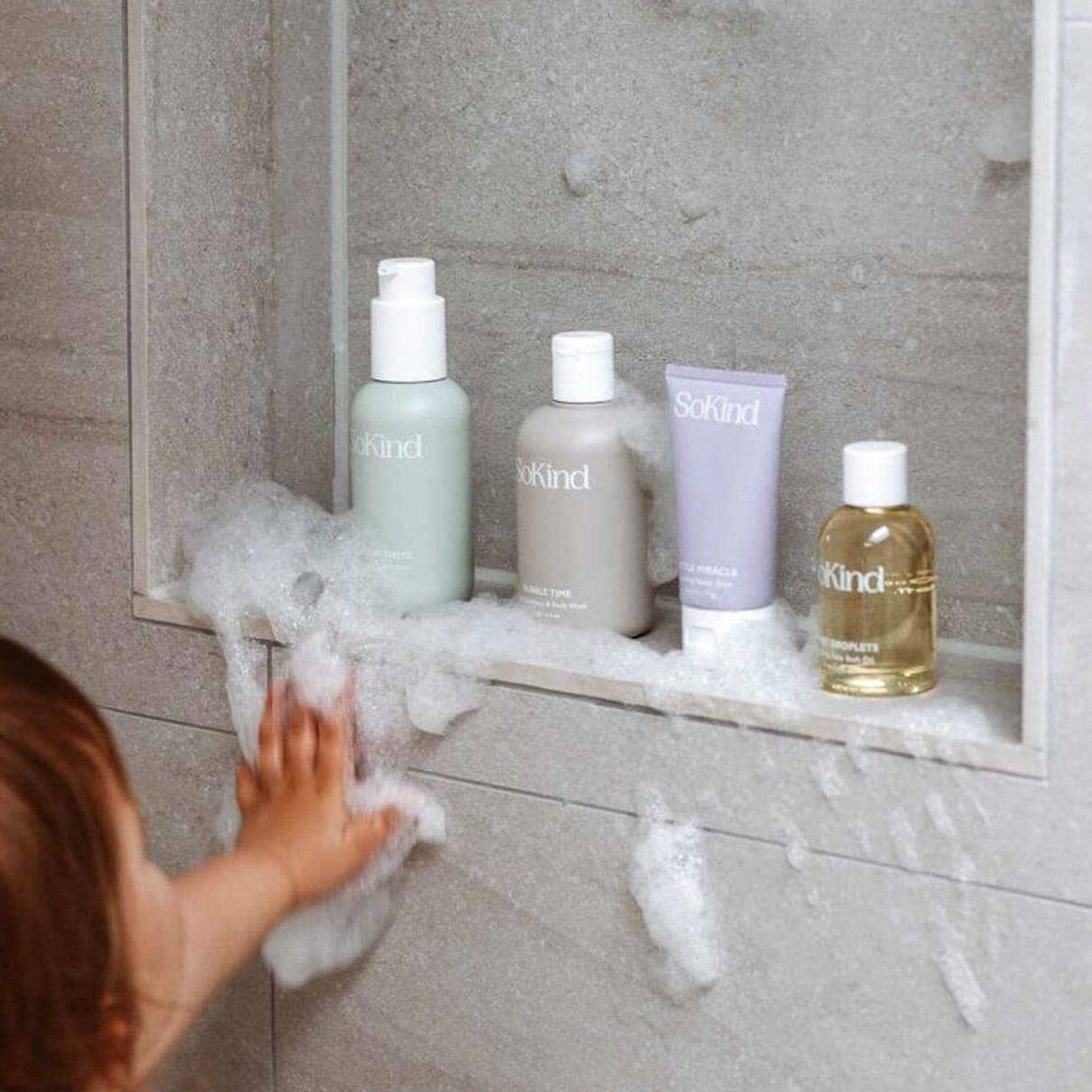 Toddler in shower with So kind skincare products on a shelf.