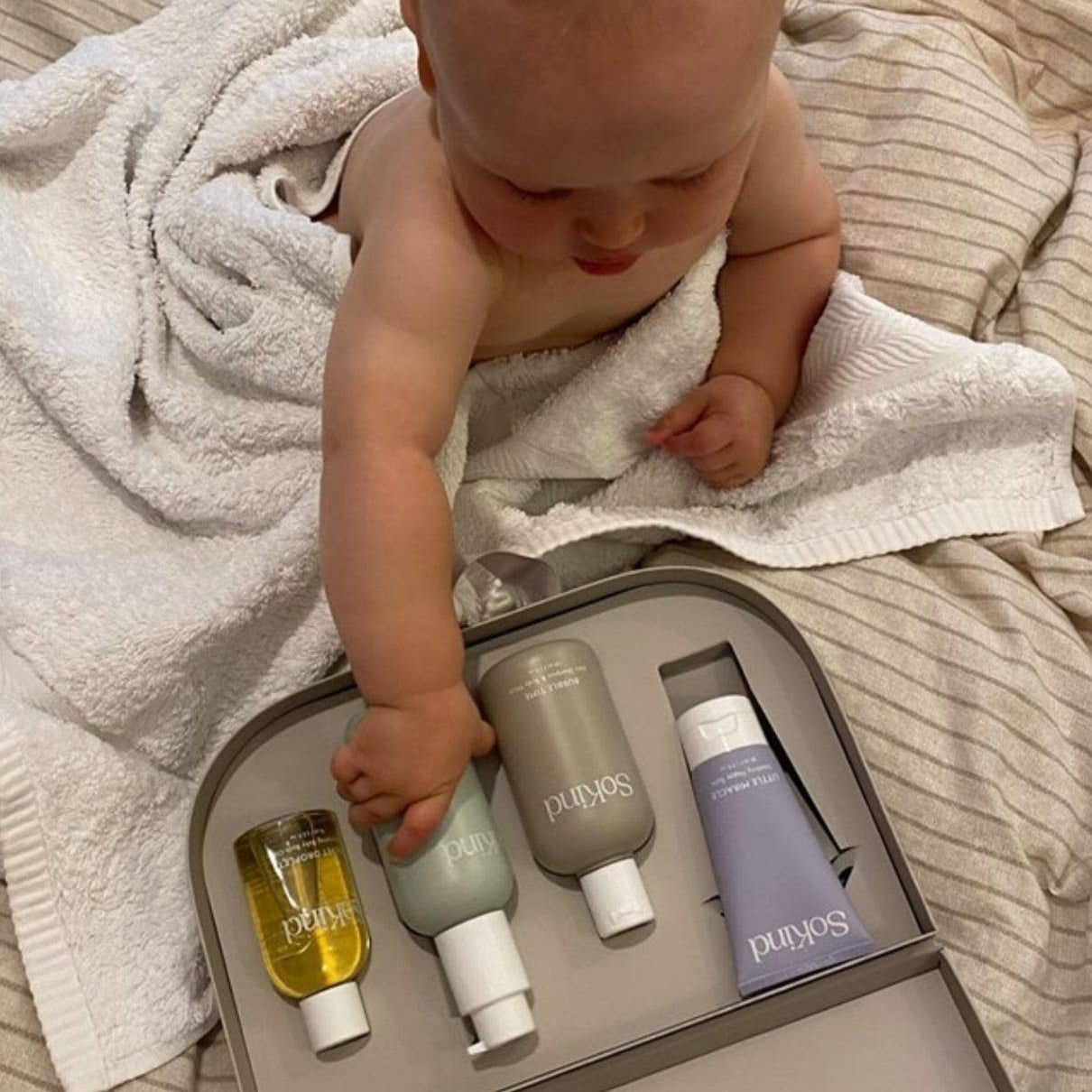 Baby interacting with So Kind skincare products on a towel