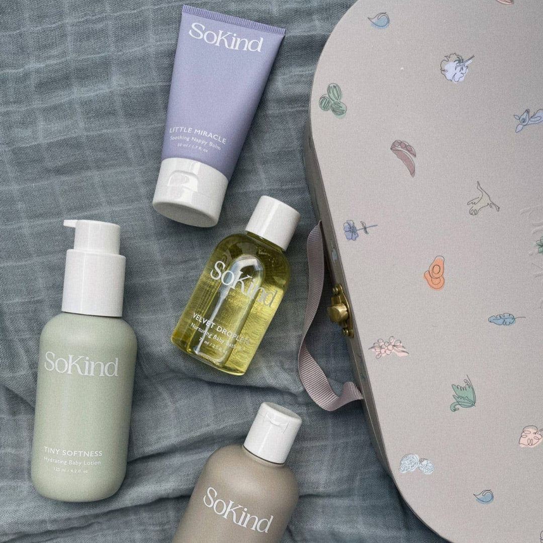 Set of SoKind skincare products on a textured surface with a decorative mat.